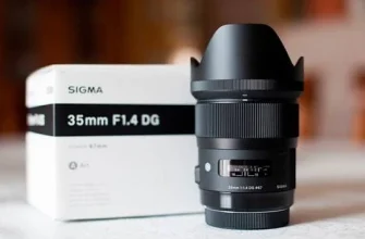 Об'єктив Sigma 35mm F1.4 DG Art чорного кольору з одягненою блендою стоїть поруч із білою фірмовою коробкою, на корпусі видно вікно шкали фокусування.
