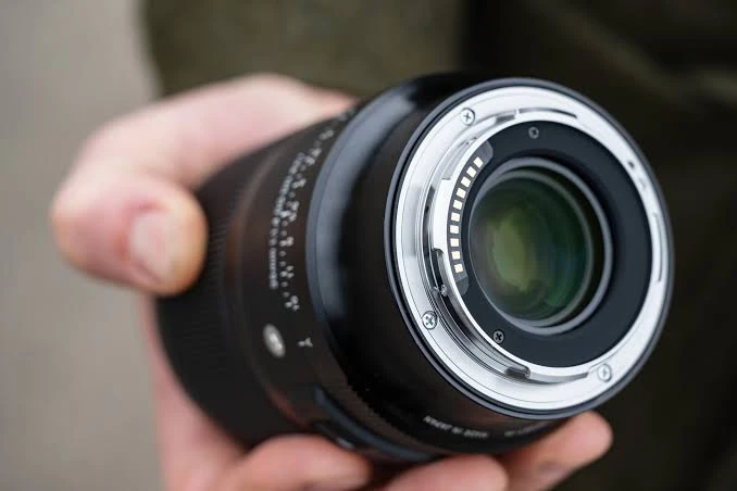Металевий байонет об'єктива Sigma в руці фотографа, видно контактну групу позолочених пінів для передачі даних на камеру.